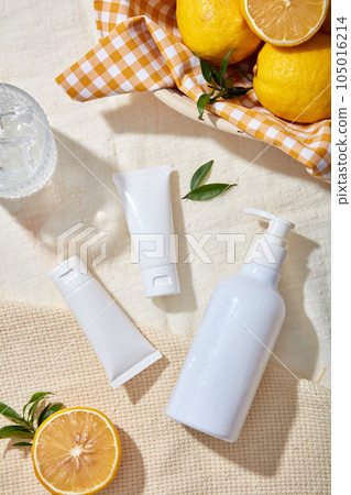 Top view of three white bottles cosmetic mockup displayed on beige fabric background with lemon, lemon slices and leaves. Scene for advertising cosmetic of lemon extract with blank space for design Top view of three white bottles cosmetic mockup displayed on beige fabric background with lemon, lemon slices and leaves. Scene for advertising cosmetic of lemon extract with blank space for design 105016214