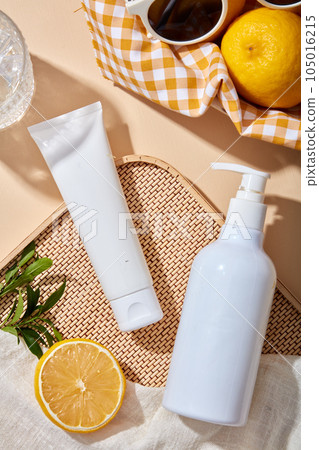 Mockup scene for advertising and branding cosmetic product of lemon extract - white plastic tube and pump bottle unbranded on beige background with lemon slices, green leaves and towel. Top view Mockup scene for advertising and branding cosmetic product of lemon extract - white plastic tube and pump bottle unbranded on beige background with lemon slices, green leaves and towel. Top view 105016215