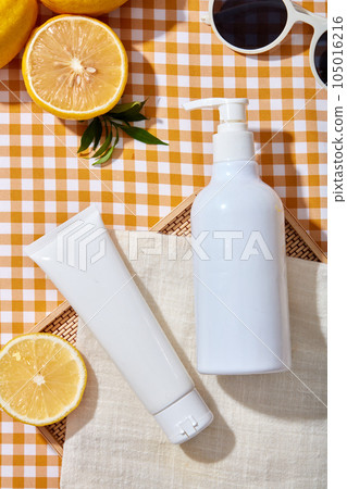 Summer concept for advertising cosmetic with vitamin C from lemon extract. Two white bottles unlabeled displayed on yellow checkered background with lemon slices and green leaves. Space for design Summer concept for advertising cosmetic with vitamin C from lemon extract. Two white bottles unlabeled displayed on yellow checkered background with lemon slices and green leaves. Space for design 105016216