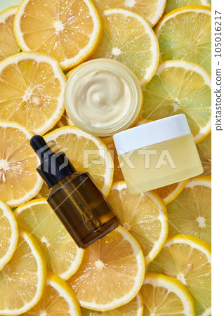Top view of an amber dropper bottle, yellow cream jar places on surface of orange slices. Mockup scene for advertising cosmetic with lemon extract. Beauty herbal skincare product concept. 105016217