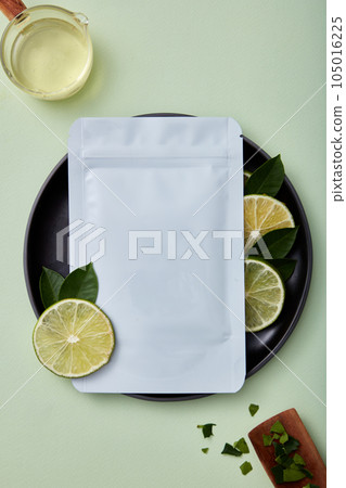 Top view of mockup of a facial sheet mask package on round plate with lime slices and green leaves decorated on pastel background. Beauty product packaging design templates based on lime 105016225