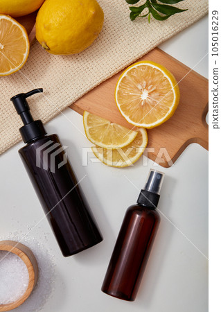 Advertising scene for skin care lemon products with ingredients from natural lemon extract. Two amber bottle unbranded displayed on white background with fresh lemon, lemon slices and green leaves. 105016229