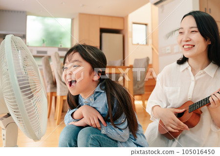 Girl singing loudly to fan and mother playing ukulele 105016450