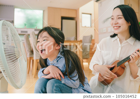 Girl singing loudly to fan and mother playing ukulele 105016452