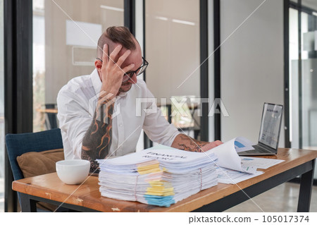 business man stress paperwork and deadline concept stressed businessman with papers and charts sitting at table in office business man stress paperwork and deadline concept stressed businessman with papers and charts sitting at table in office 105017374