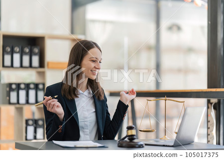 Female lawyer happily working on chatting via laptop with checks clients' contracts with hammer and legal book scales Female lawyer happily working on chatting via laptop with checks clients' contracts with hammer and legal book scales 105017375