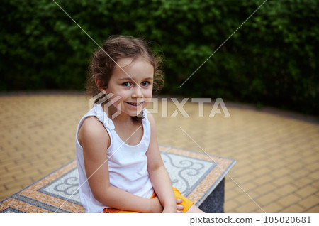 Caucasian adorable little child girl 4 years smiling looking at camera, sitting on a mosaic bench in the city park Caucasian adorable little child girl 4 years smiling looking at camera, sitting on a mosaic bench in the city park 105020681