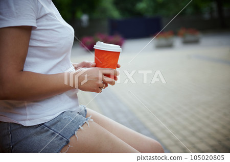 Cropped view of female hands with bright orange disposable cardboard cup of takeaway hot drink. Sustainability Lifestyle Cropped view of female hands with bright orange disposable cardboard cup of takeaway hot drink. Sustainability Lifestyle 105020805