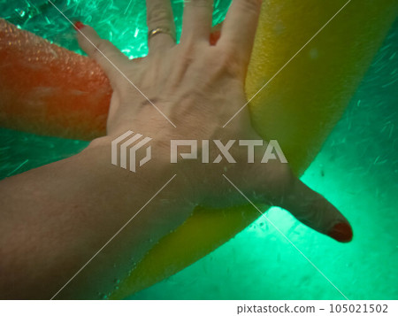 Woman's hand reaches through swimming pool water for a pool noodle Woman's hand reaches through swimming pool water for a pool noodle 105021502