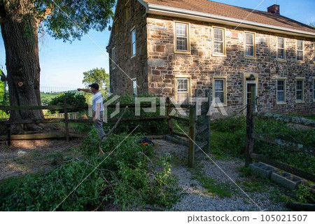 Off center man lsees fallen branches storm damage by old stone house 105021507