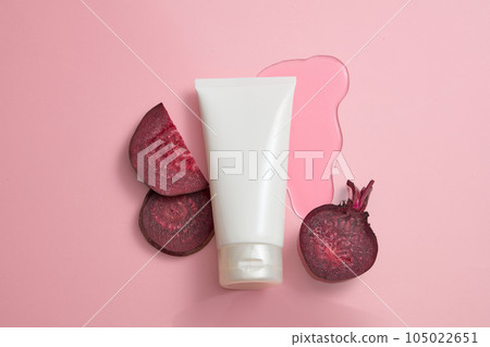 Minimalist advertisement scene for cosmetic with natural extract - white plastic tube unlabeled decorated with fresh beetroot slices on pink background. Top view, blank space for design 105022651