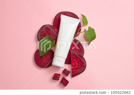 Concept for advertising organic cosmetic with natural extract. White plastic tube decorated with beetroot slices and fish mint leaves on a pink background. Top view, blank space for design 105022662