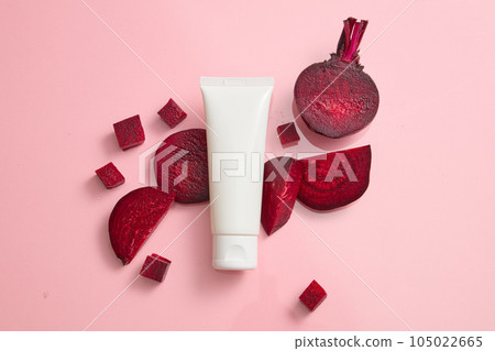 Scene for advertising and branding cosmetic with beetroot ingredient. An empty white plastic tube on pink background with beet slices. Beetroot contains many important nutrients good for beauty 105022665
