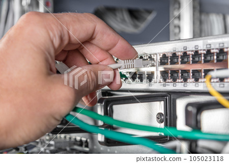 closeup of hand of administrator connecting network cable into switch closeup of hand of administrator connecting network cable into switch 105023118