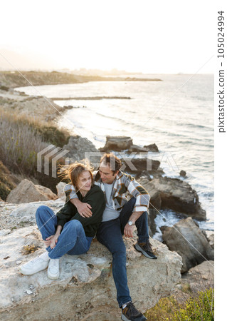 Portrait of a middle-aged couple sitting on a rock at the beach in Cyprus. They are wearing casual clothes Portrait of a middle-aged couple sitting on a rock at the beach in Cyprus. They are wearing casual clothes 105024994
