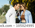 Young happy couple outdoors drinking cold drink from glass bottle with straw. Side view of man and woman drinking soft drink and smiling. 105024995