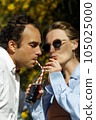 Young happy couple outdoors drinking cold drink from glass bottle with straw. Side view of man and woman drinking soft drink and smiling. 105025000