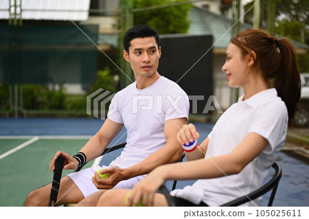 Experienced male tennis coach giving instructions to his student, standing by net at the outdoor tennis court 105025611