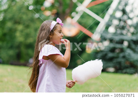 Funny girl in pink dress eats cotton candy in summer in the park 105027071
