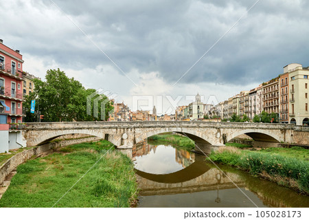 Colorful yellow and orange houses and bridge Pont de Sant Agusti reflected in water river Onyar, in Girona, Catalonia, Spain. Church of Sant Feliu and Saint Mary Cathedral at background. BRIDGE in the Colorful yellow and orange houses and bridge Pont de Sant Agusti reflected in water river Onyar, in Girona, Catalonia, Spain. Church of Sant Feliu and Saint Mary Cathedral at background. BRIDGE in the 105028173