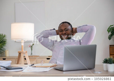 Smiling black man using laptop at home in living room. Happy mature businessman send email and working at home. African american man typing on computer with paperworks and documents on table 105028861