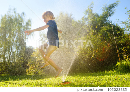Funny little boy playing with garden sprinkler in sunny backyard. Preschooler child laughing, jumping and having fun with spray of water. Funny little boy playing with garden sprinkler in sunny backyard. Preschooler child laughing, jumping and having fun with spray of water. 105028885