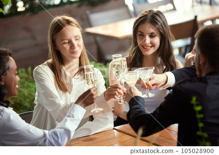 Cheerful young people, colleagues meeting in restaurant after work, celebrating project, drinking champagne and talking Cheerful young people, colleagues meeting in restaurant after work, celebrating project, drinking champagne and talking 105028900