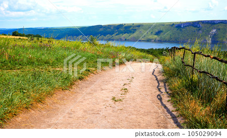 Rural dirt road to the river among fields and hills on a sunny day 105029094
