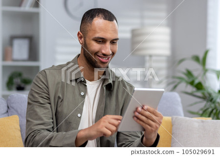 Close-up photo. Young hispanic man using tablet at home. dials, chats, talks via video call. 105029691