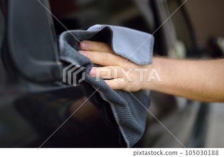 A mature man cleans his car with rag. Driver washes the glass of his car using microfiber washcloth. 105030188