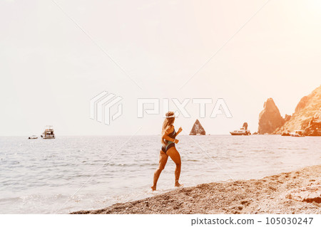Woman travel summer sea. A happy tourist in a blue bikini enjoying the scenic view of the sea and volcanic mountains while taking pictures to capture the memories of her travel adventure. 105030247