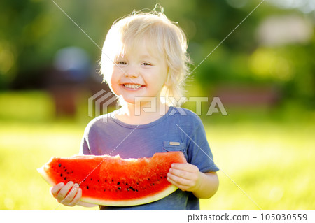 Cute caucasian little boy with blond hairs eating fresh watermelon outdoors 105030559