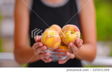 woman holding bowl of fresh peaches in her hands while standing in garden 105031309