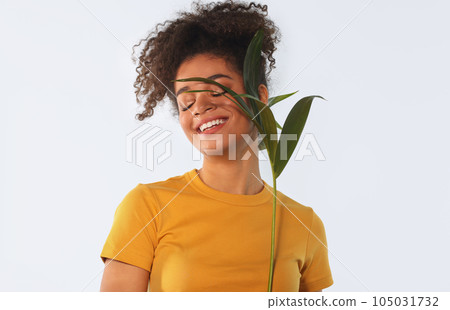 Young happy joyful african american woman holding green tropical plant and smiling with closed eyes Young happy joyful african american woman holding green tropical plant and smiling with closed eyes 105031732