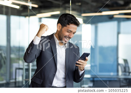 Young arab businessman happy celebrating victory reading news online, man got win holding joyfully hand up triumph gesture. 105035225