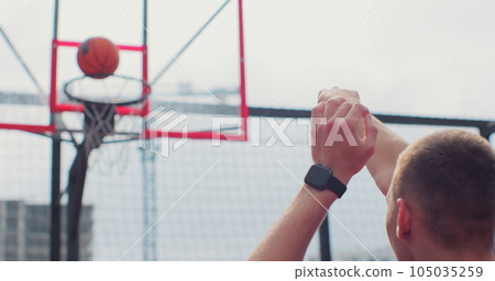 Back view of man player throwing ball in a basketball hoop. Successfully throws ball into the basket ring. Sport lifestyle. 105035259