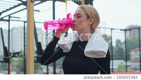 Portrait of a woman drinking water from the pink sport bottle. Fit girl drink water from bottle. Rest after hard workout. 105035302