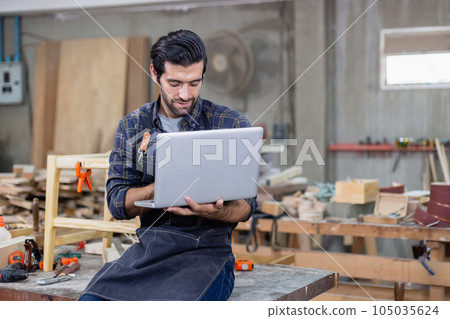 young carpenter caucasian man with laptop make drawing on wood to design at workspace. young carpenter caucasian man with laptop make drawing on wood to design at workspace. 105035624