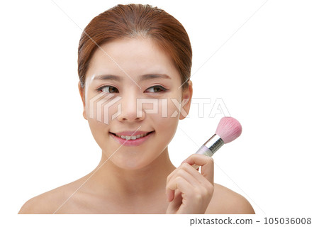clean-skinned female model holding a makeup brush against a white background 105036008