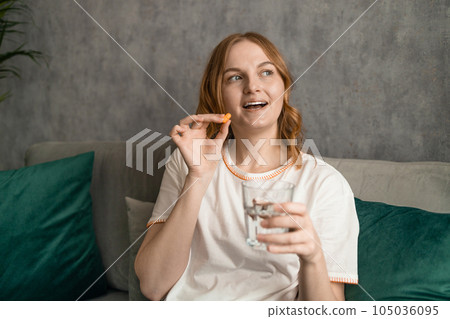 Beautiful young woman taking pills, sitting on couch at home. High quality photo Beautiful young woman taking pills, sitting on couch at home. High quality photo 105036095
