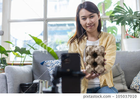 Asian female holding paper boxes live stream talk on smartphone introducing waste sorting. Asian female holding paper boxes live stream talk on smartphone introducing waste sorting. 105037010
