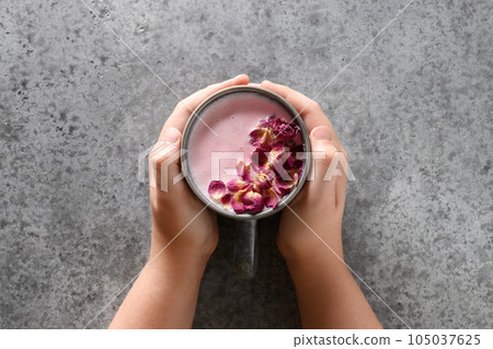 Rose moon milk in cup for a better sleep in child hands on grey. Ayurveda warm drink. Nice in case of sleeplessness. 105037625