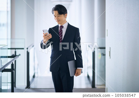A middle-class businessman in a suit who operates a smartphone in the office 105038547