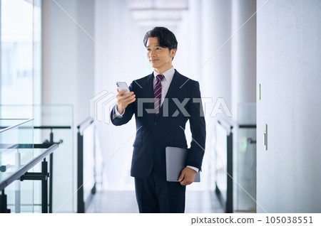 A middle-class businessman in a suit who operates a smartphone in the office 105038551