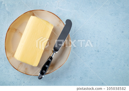 A block of butter with a knife on a plate, overhead flat lay shot A block of butter with a knife on a plate, overhead flat lay shot 105038582