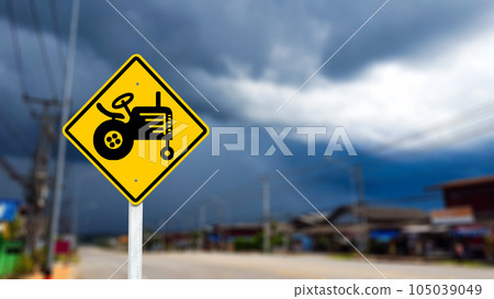 Graphic of tractor on yellow sign on blurred background to warn traffic to aware of agricultural vehicles crossing the street Graphic of tractor on yellow sign on blurred background to warn traffic to aware of agricultural vehicles crossing the street 105039049