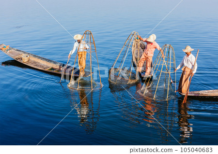 Myanmar travel attraction landmark - three traditional Burmese fishermen balancing with fishing net at Inle lake in Myanmar famous for their distinctive one legged rowing style Myanmar travel attraction landmark - three traditional Burmese fishermen balancing with fishing net at Inle lake in Myanmar famous for their distinctive one legged rowing style 105040683