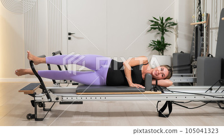 A young pregnant woman is practicing Pilates on a reformer. Exercises for the expectant mother A young pregnant woman is practicing Pilates on a reformer. Exercises for the expectant mother 105041323