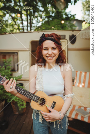 Happy hippie girl is having a good time with playing on guitar in camper trailer. Holiday, vacation, trip concept. Happy hippie girl is having a good time with playing on guitar in camper trailer. Holiday, vacation, trip concept. 105041402