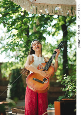 Happy hippie girl is having a good time with playing on guitar in camper trailer. Holiday, vacation, trip concept. Happy hippie girl is having a good time with playing on guitar in camper trailer. Holiday, vacation, trip concept. 105041420